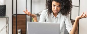 Woman looking exasperated and confused in front of a laptop.